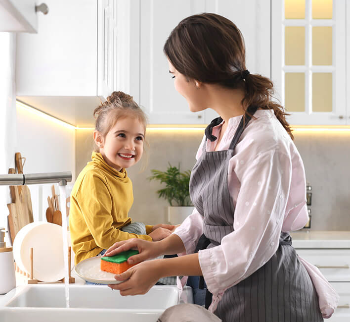 A woman and child at a kitchen sink, smiling